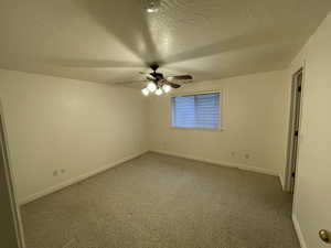 Empty room with a textured ceiling, carpet floors, and ceiling fan