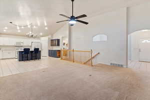 Unfurnished living room with light tile patterned floors, high vaulted ceiling, light colored carpet, a chandelier, and a ceiling fan