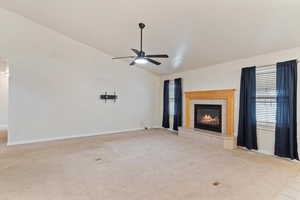 Unfurnished living room featuring lofted ceiling, a fireplace, light colored carpet, and ceiling fan