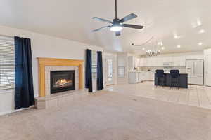 Living area with lofted ceiling, a fireplace, a chandelier, light colored carpet, and a ceiling fan