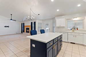 Kitchen featuring white cabinets, a tiled fireplace, a center island, vaulted ceiling, and white dishwasher