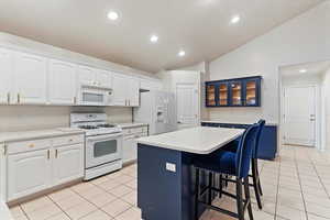 Kitchen featuring recessed lighting, a kitchen bar, white appliances, light countertops, and glass insert cabinets