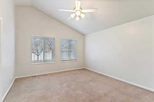 Spare room featuring vaulted ceiling, light colored carpet, and a ceiling fan