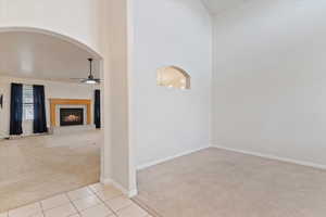 Empty room with light carpet, a tile fireplace, ceiling fan, arched walkways, and light tile patterned floors