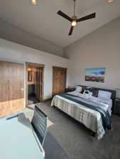 Carpeted bedroom with ensuite bathroom, high vaulted ceiling, and ceiling fan