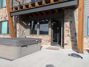 View of exterior entry featuring stone siding, a patio area, and a hot tub