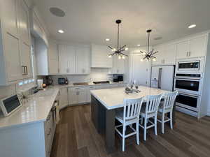Kitchen featuring white cabinetry, hanging light fixtures, a center island, a kitchen bar, and dark wood-style floors