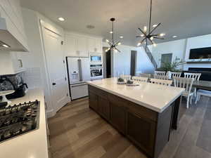 Kitchen featuring hanging light fixtures, appliances with stainless steel finishes, dark wood finished floors, white cabinetry, and dark brown cabinets