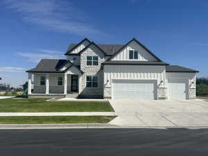 View of front facade with stone siding, board and batten siding, covered porch, and a front lawn
