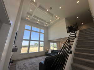 Living area with coffered ceiling, beam ceiling, stairs, recessed lighting, and a towering ceiling