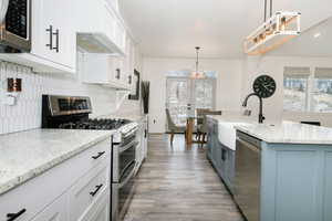 Kitchen with appliances with stainless steel finishes, white cabinetry, decorative light fixtures, and light stone counters