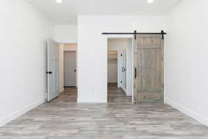 Unfurnished bedroom with a spacious closet, light wood finished floors, a barn door, and recessed lighting