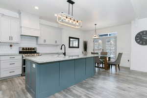 Kitchen with granite countertops, range with two ovens, pendant lighting, a kitchen island with sink, and white cabinetry