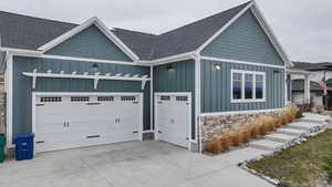 View of front facade featuring board and batten siding, a garage, a shingled roof, stone siding, and driveway