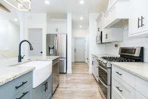 Kitchen featuring stainless steel appliances, light wood finished floors, white cabinetry, light stone countertops, and recessed lighting