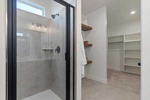 Full bath with a walk in closet, a shower stall, and light tile patterned floors