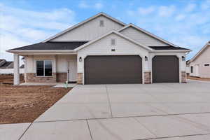 Craftsman-style house featuring stone siding, a garage, board and batten siding, concrete driveway, and a shingled roof