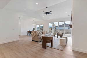 Living room with a ceiling fan, lofted ceiling, light wood finished floors, and a chandelier