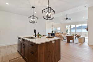 Kitchen featuring open floor plan, light wood-style floors, ceiling fan, light stone counters, and an island with sink
