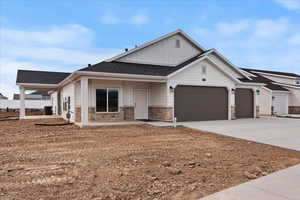 View of front of house with an attached garage, board and batten siding, concrete driveway, and stone siding