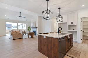 Dual tone kitchen with two tone color scheme, a kitchen island with sink, a fireplace, ceiling fan, and dishwasher