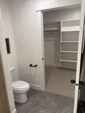 Photos are of staged model home.  Primary Suite Bathroom with dark marble finish flooring, dark carpet, and a walk in closet