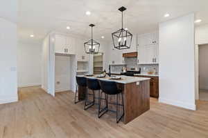 Kitchen featuring a breakfast bar area, a center island with sink, two tone cabinets, light wood finished floors, and gas stove