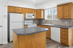 Kitchen featuring white appliances, a center island, tasteful backsplash, and dark countertops