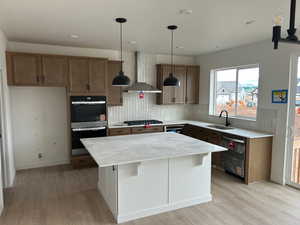 Kitchen featuring wall chimney range hood, a center island, appliances with stainless steel finishes, and decorative backsplash