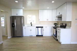 Kitchen with stainless steel appliances, white cabinetry, under cabinet range hood, recessed lighting, and light wood-type flooring