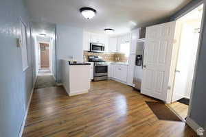Kitchen featuring white cabinets, appliances with stainless steel finishes, tasteful backsplash, and dark wood-style flooring