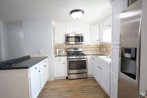 Kitchen with appliances with stainless steel finishes, white cabinets, light wood finished floors, backsplash, and a peninsula