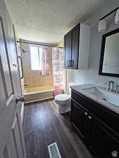 Bathroom with dark wood-style floors, vanity, shower / bath combination with curtain, and a textured ceiling