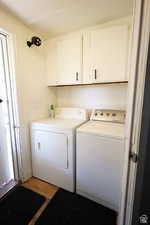 Washroom with cabinet space, washing machine and clothes dryer, and light wood-style flooring