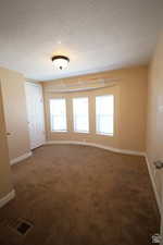 Unfurnished room featuring a textured ceiling, healthy amount of natural light, and dark colored carpet