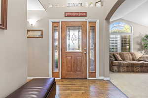 Carpeted foyer featuring vaulted ceiling, plenty of natural light, wood finished floors, and arched walkways