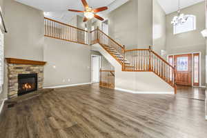 Unfurnished living room with wood finished floors, stairs, high vaulted ceiling, a stone fireplace, and a ceiling fan