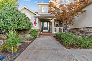 Property entrance with stone siding, stucco siding, a shingled roof, and a porch