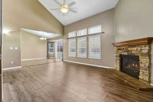 Unfurnished living room featuring high vaulted ceiling, wood finished floors, a stone fireplace, a chandelier, and ceiling fan