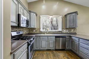 Kitchen featuring stainless steel appliances, gray cabinets, lofted ceiling, dark wood-style floors, and tasteful backsplash