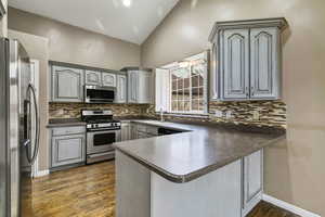 Kitchen featuring dark countertops, appliances with stainless steel finishes, a peninsula, gray cabinets, and dark wood-style flooring