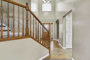 Foyer entrance with arched walkways, wood finished floors, a high ceiling, stairway, and a chandelier