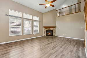 Unfurnished living room with high vaulted ceiling, light wood finished floors, ceiling fan, and a fireplace