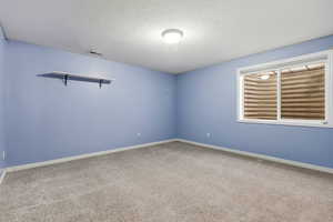 Carpeted empty room featuring a textured ceiling and baseboards