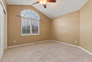 Empty room featuring vaulted ceiling, light carpet, and a ceiling fan