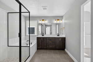 Full bathroom featuring a textured ceiling, a bath, double vanity, light tile patterned floors, and a stall shower
