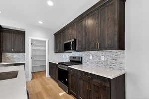 Kitchen with dark brown cabinetry, decorative backsplash, stainless steel appliances, light wood-style flooring, and light stone countertops