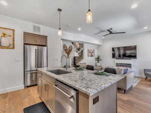 Kitchen with decorative light fixtures, light stone counters, appliances with stainless steel finishes, a glass covered fireplace, and light wood finished floors