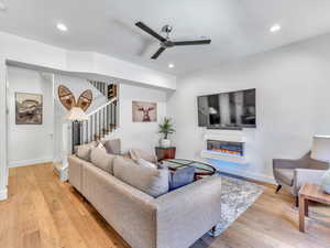 Living room featuring a glass covered fireplace, ceiling fan, light wood-style flooring, stairway, and recessed lighting
