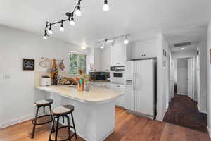 Kitchen featuring white appliances, a peninsula, light countertops, white cabinets, and light wood-type flooring